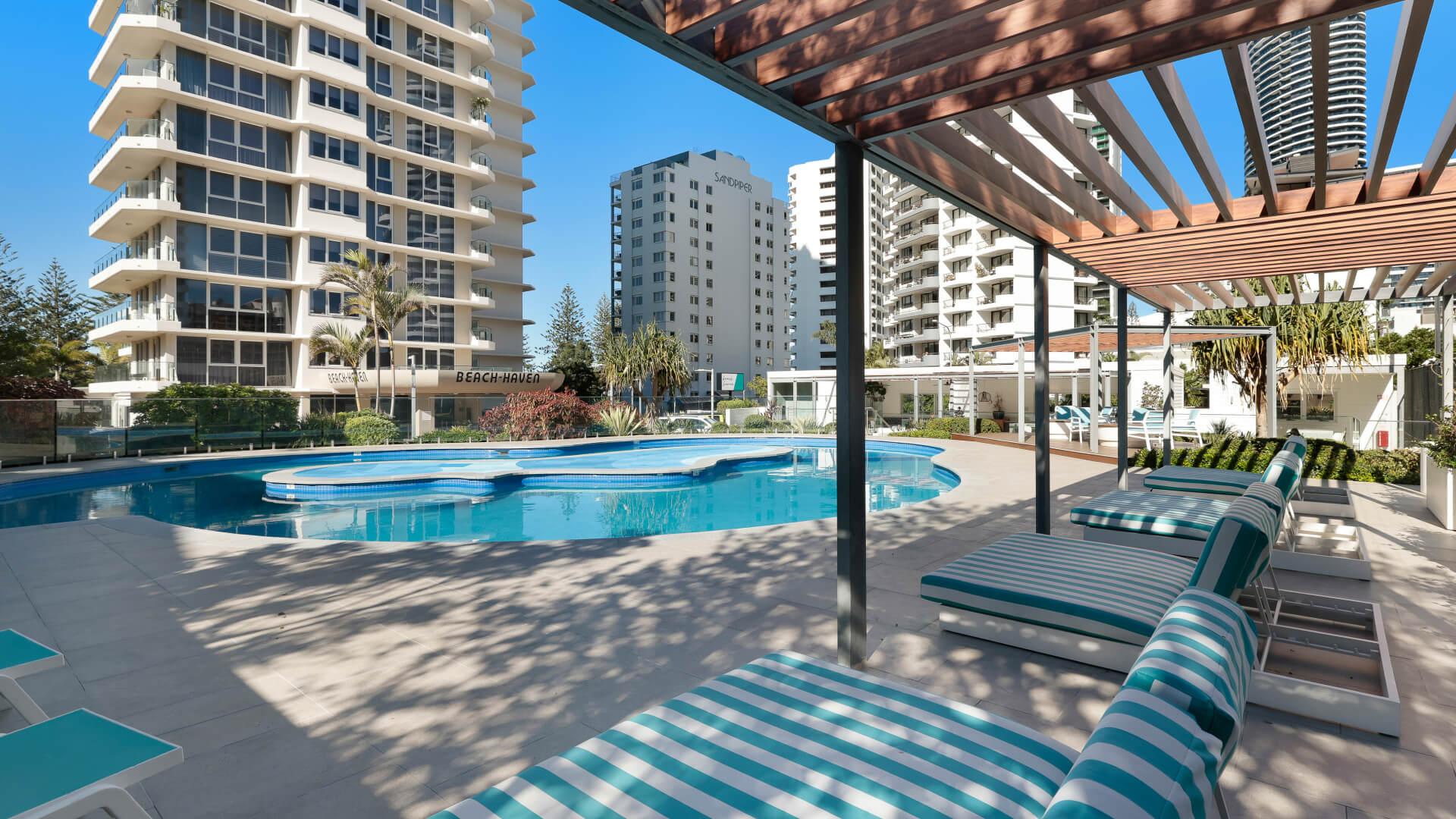 Image of a modern utdoor pool with sun lounges around it in shade at ULTIQA Beach Haven