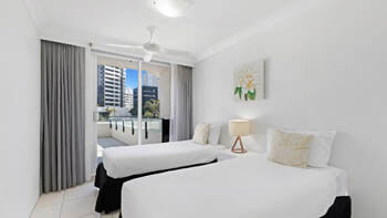 Second bedroom at ULTIQA Beach Haven on Broadbeach with two single beds, bedside table and lamp, and balcony access via sliding doors.