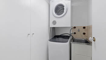 Laundry at ULTIQA Beach Haven on Broadbeach with stacked dryer, washing machine, utility sink, and built-in storage cupboards.