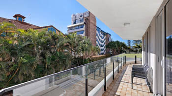 Private balcony at ULTIQA Beach Haven on Broadbeach with tiled flooring, outdoor chairs, glass balustrade, and views of greenery and surrounding buildings.