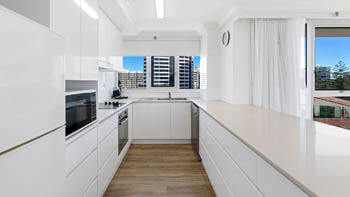 Galley-style kitchen at ULTIQA Beach Haven on Broadbeach with white cabinetry, built-in oven, dishwasher, and a window with city views.