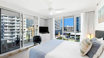 Main bedroom at ULTIQA Beach Haven on Broadbeach with a queen bed, bedside lighting, and balcony access with city skyline views.