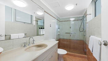 Bathroom at ULTIQA Beach Haven on Broadbeach with vanity, mirror, toilet, and a large walk-in glass shower with grab rail.