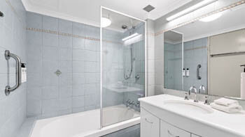 Bathroom with shower over bath, light blue tiled walls, vanity and mirrored cabinet at ULTIQA Beach Haven on Broadbeach.