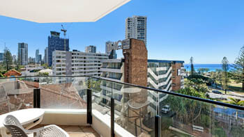 Balcony with outdoor table and chairs behind a glass balustrade, overlooking the city skyline with the ocean in the distance at ULTIQA Beach Haven on Broadbeach.