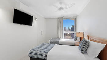 Second bedroom with clean white bedding on two single beds and a tv in front of it at ULTIQA Beach Haven on Broadbeach.