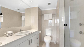 Clean bathroom with a toilet, sink, mirror and a walk in shower at ULTIQA Beach Haven on Broadbeach.