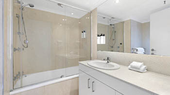 Bathroom with a combined bath and shower as well as a sink and clean white towels next to it at ULTIQA Beach Haven on Broadbeach.