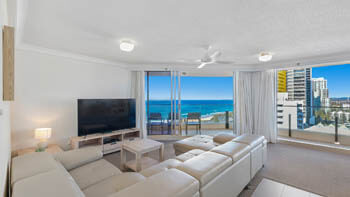Living room with white leather couch and a modern TV and stunning views in the background at ULTIQA Beach Haven on Broadbeach.