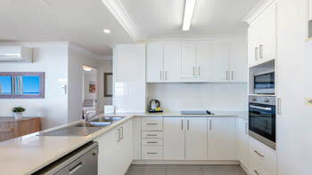 Modern white fully equipped kitchen with dishwasher, microwave and over at ULTIQA Beach Haven on Broadbeach.
