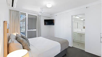 Master bedroom with a large king bed, tv in the corner and entrance to a bathroom at ULTIQA Beach Haven on Broadbeach.