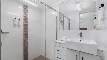 Bathroom with clean white tiles, a walk-in shower and a big sink at ULTIQA Beach Haven on Broadbeach.