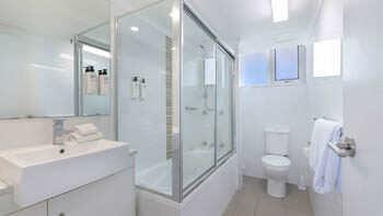 Bathroom with clean white tiles, a walk-in shower and a big sink at ULTIQA Beach Haven on Broadbeach.