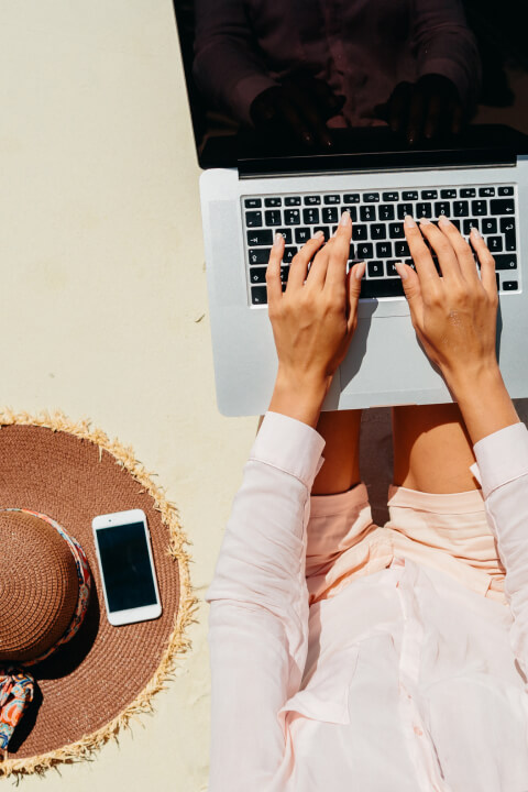 Person working on a laptop beside a pool, enjoying a relaxed and sunny setting.