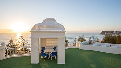Rooftop seating area at ULTIQA Burleigh with ocean views, surrounded by greenery and overlooking the coastline at sunset.