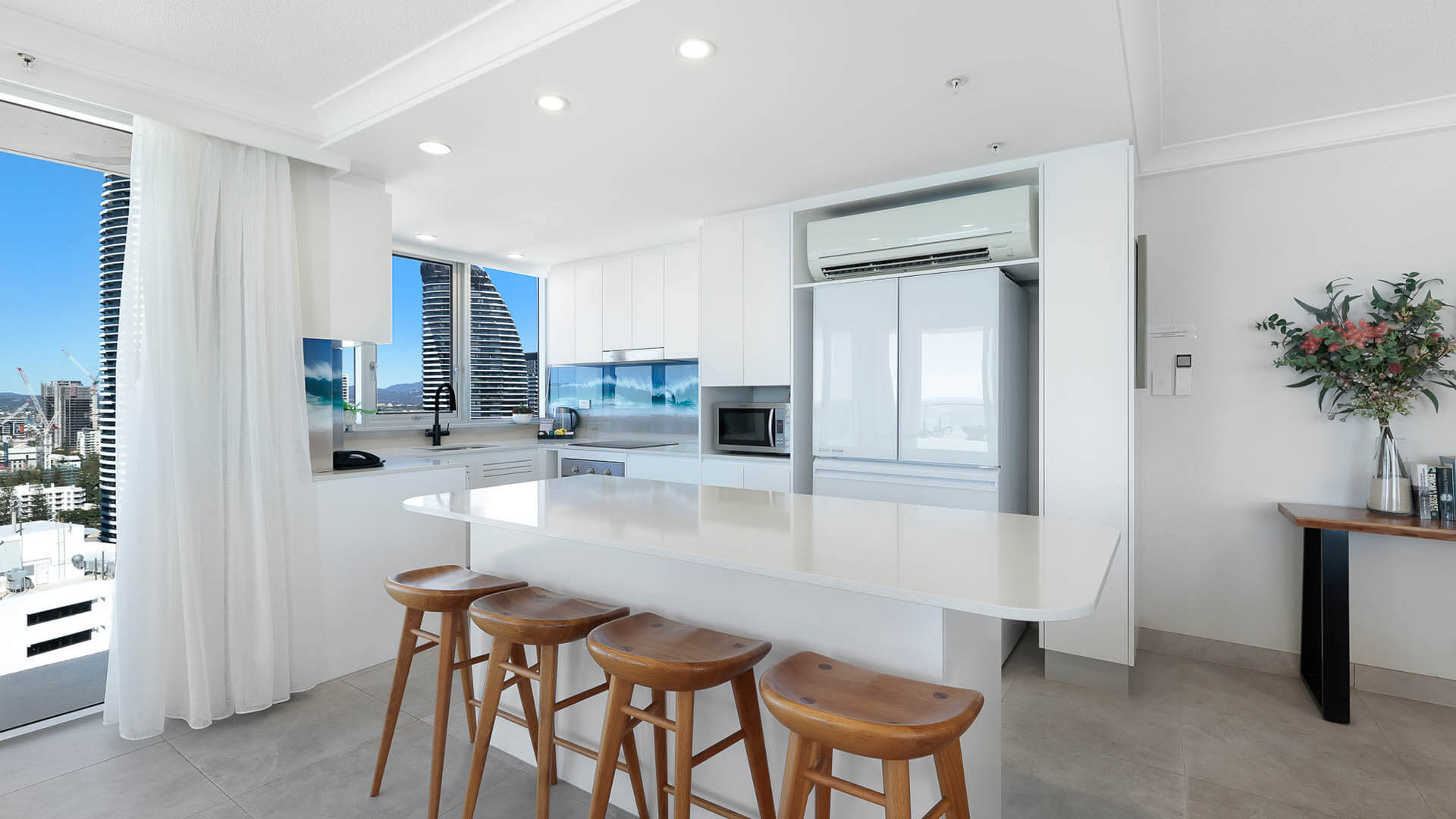 Modern kitchen with island bench, timber stools, and skyline views.